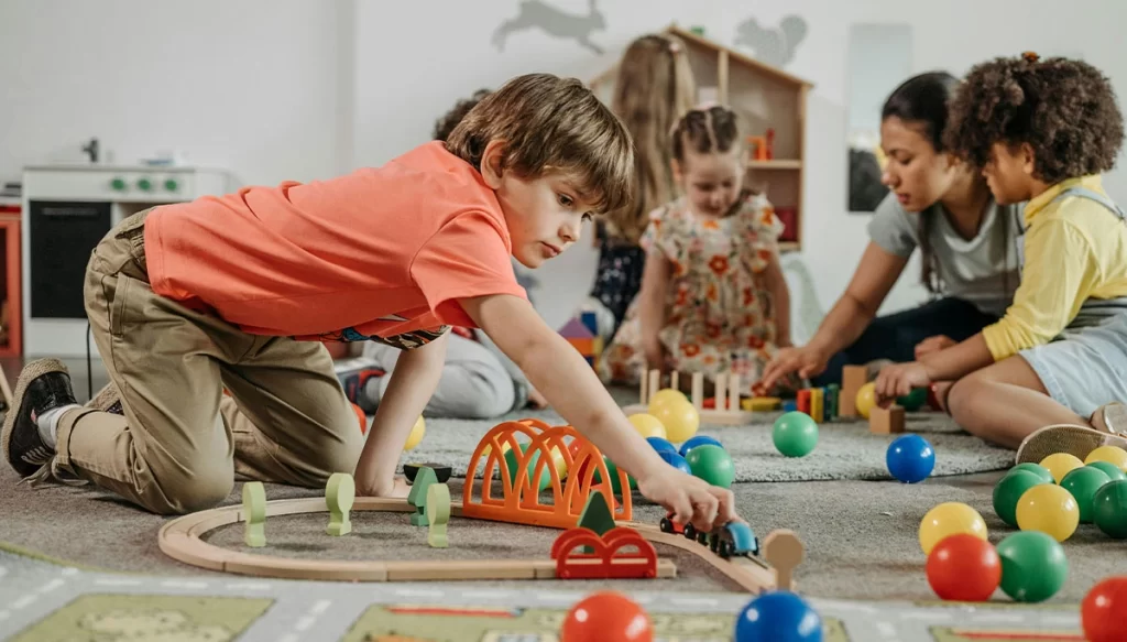 young boy pushes a toy vehicle as children play in the background