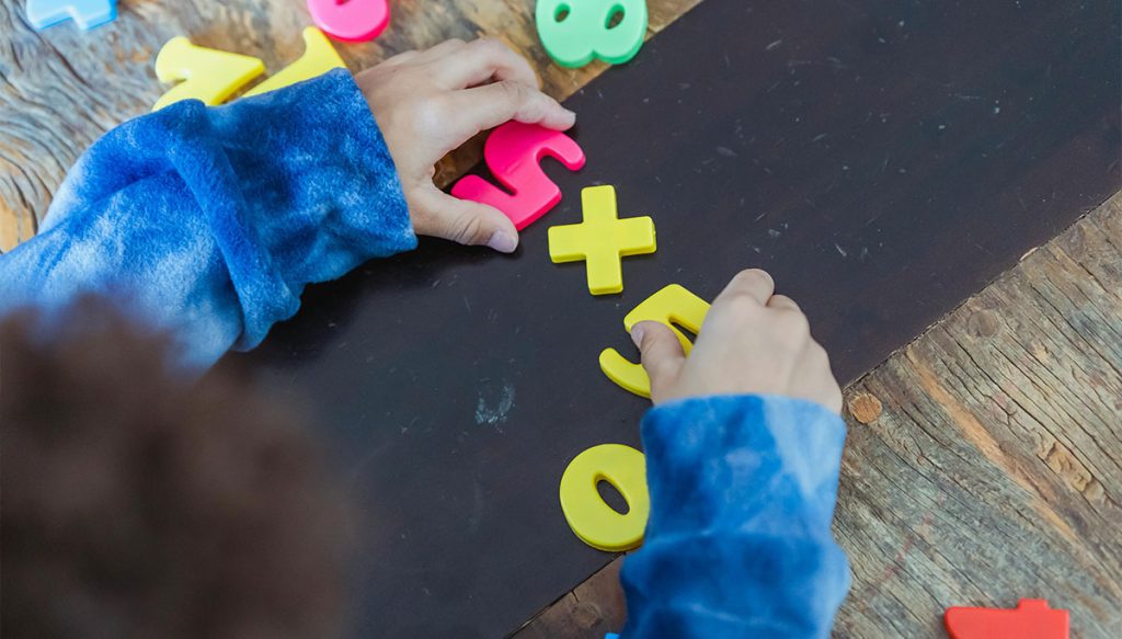 young child's hands arranging plastic numbers on a table.
