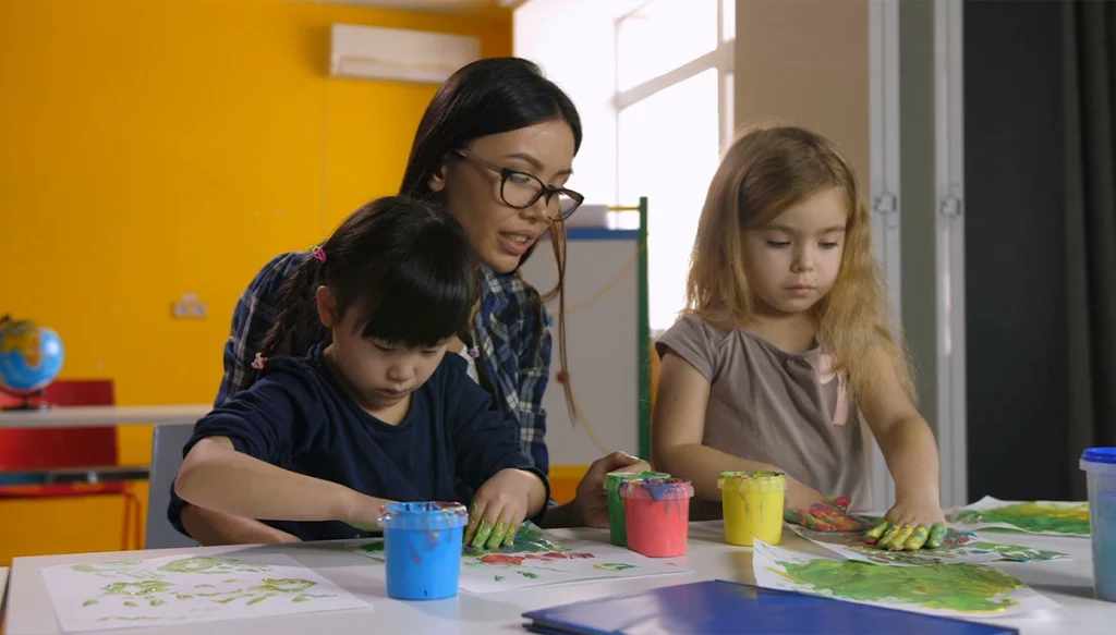 teacher assisting two female students who are finger painting