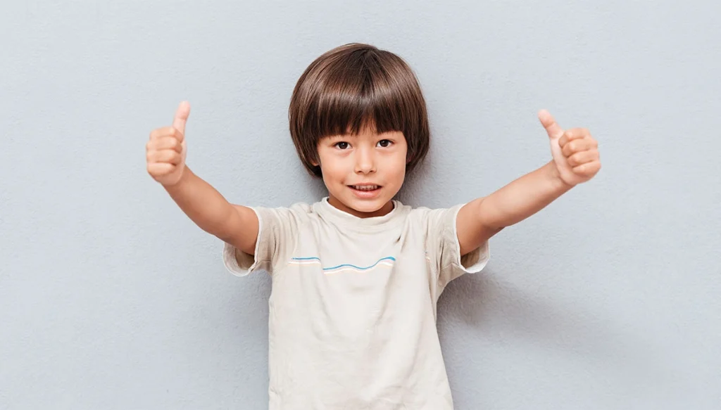 young boy holding two thumbs up and smiling