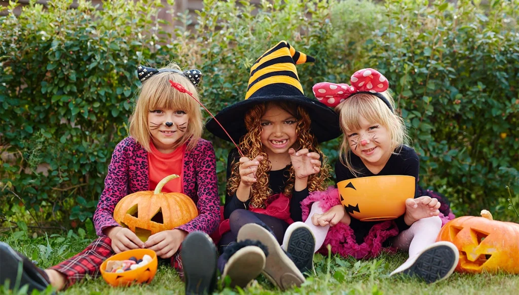 girls in halloween costumes holding pumpkin style containers