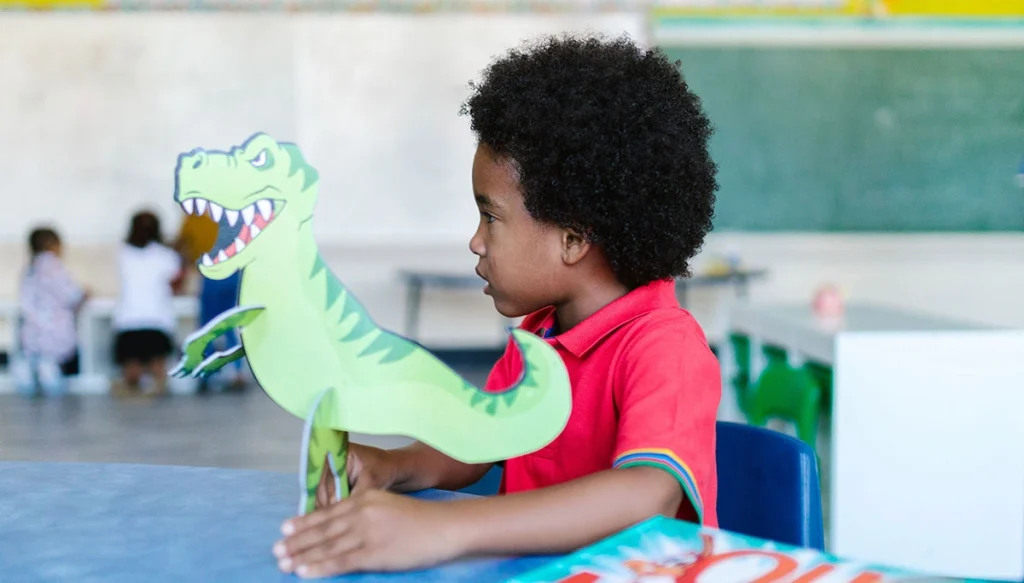 Young boy in a classroom playing with a dinosaur toy, highlighting learning fun