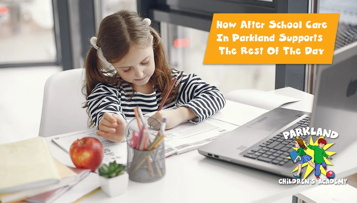 young girl sitting at a desk filled with books pencils rulers an apple and a laptop while writing in a book